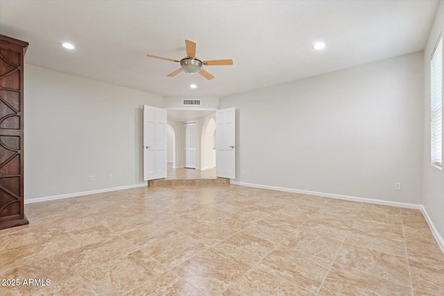 empty room featuring arched walkways, a ceiling fan, baseboards, recessed lighting, and visible vents