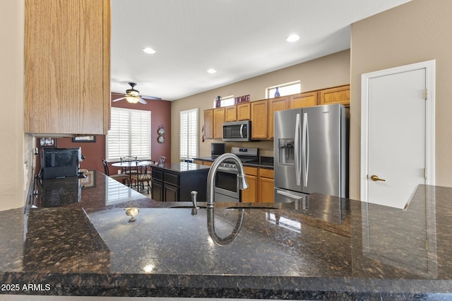 kitchen featuring recessed lighting, appliances with stainless steel finishes, a sink, dark stone counters, and a peninsula