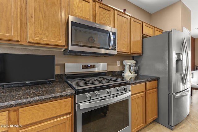 kitchen with appliances with stainless steel finishes, dark stone counters, and light tile patterned flooring