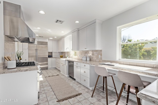 kitchen featuring a breakfast bar, white cabinets, island exhaust hood, light stone countertops, and backsplash