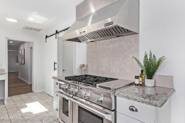 kitchen with white cabinetry, tasteful backsplash, a barn door, range with two ovens, and wall chimney range hood