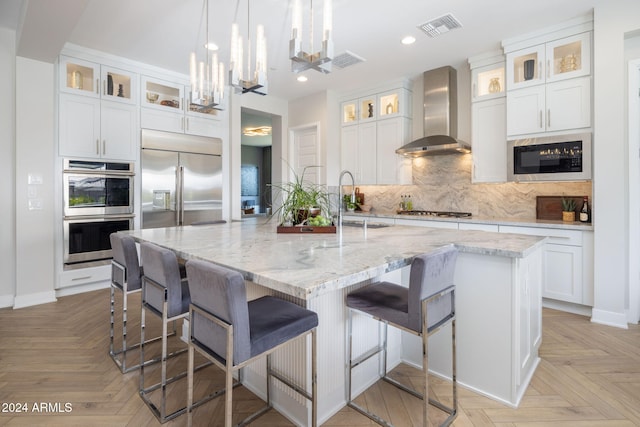 kitchen featuring white cabinetry, wall chimney range hood, built in appliances, and a spacious island