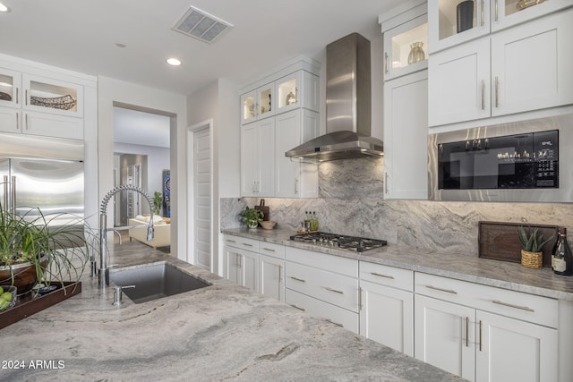 kitchen with white cabinetry, sink, built in appliances, light stone countertops, and wall chimney exhaust hood