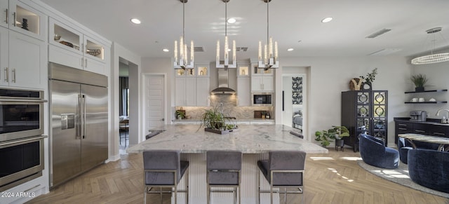 kitchen with white cabinets, a kitchen bar, built in appliances, light parquet flooring, and light stone countertops