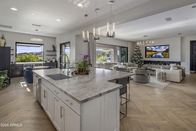 kitchen featuring sink, white cabinetry, a kitchen island with sink, hanging light fixtures, and light stone counters