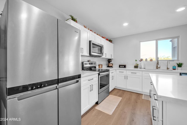 kitchen featuring white cabinetry, sink, light hardwood / wood-style floors, and appliances with stainless steel finishes