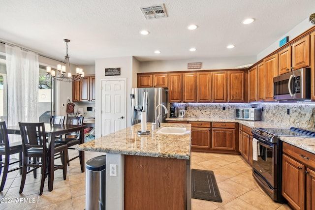 kitchen featuring stainless steel appliances, a notable chandelier, sink, an island with sink, and decorative light fixtures