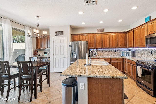 kitchen featuring sink, appliances with stainless steel finishes, an island with sink, hanging light fixtures, and a chandelier