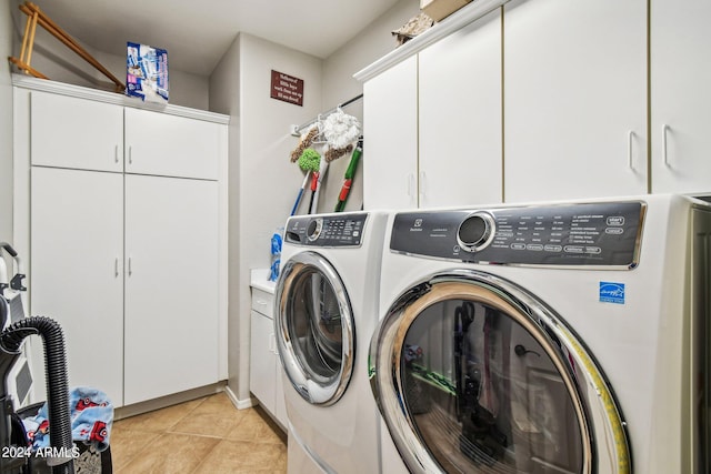 clothes washing area featuring washing machine and clothes dryer, light tile patterned flooring, and cabinets