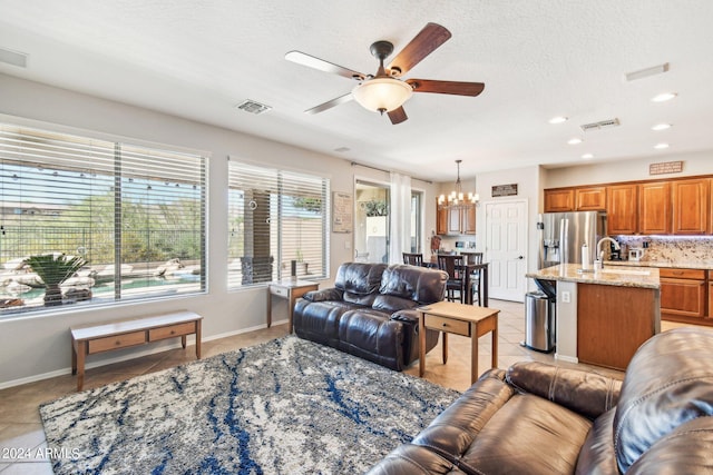 living room featuring a textured ceiling, ceiling fan with notable chandelier, light tile patterned flooring, and sink