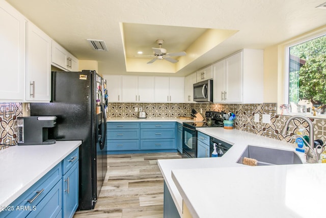 kitchen with visible vents, black appliances, a sink, white cabinets, and a raised ceiling