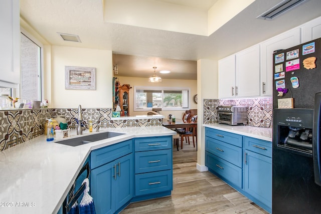 kitchen featuring blue cabinets, a sink, black fridge with ice dispenser, backsplash, and white cabinets