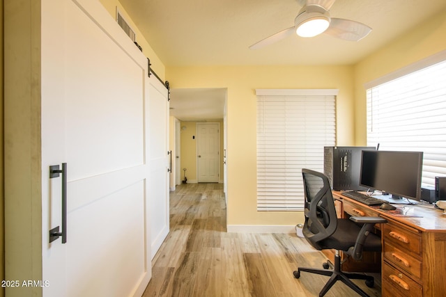 office space featuring light wood-type flooring, visible vents, a barn door, baseboards, and ceiling fan