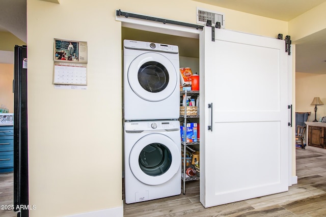 clothes washing area with visible vents, a barn door, stacked washer and dryer, laundry area, and light wood-style floors