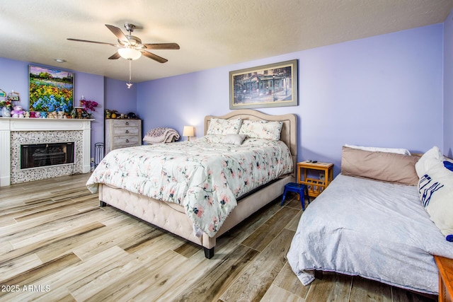 bedroom with a fireplace, a textured ceiling, ceiling fan, and wood finished floors