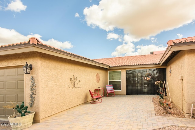 view of exterior entry with a tile roof, a patio area, a garage, and stucco siding