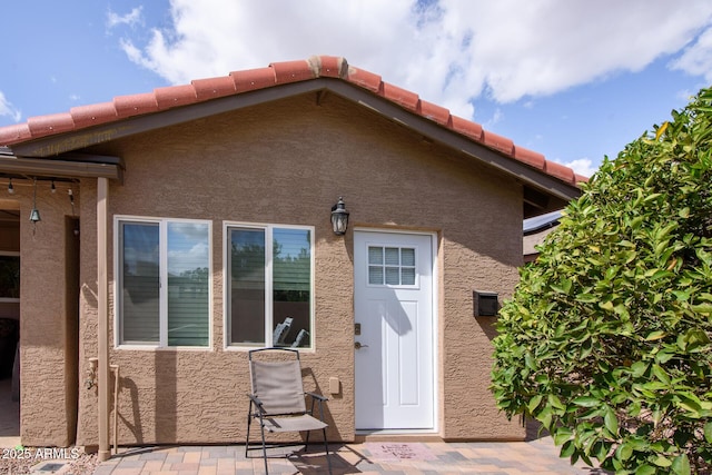 rear view of property featuring stucco siding, a patio, and a tiled roof