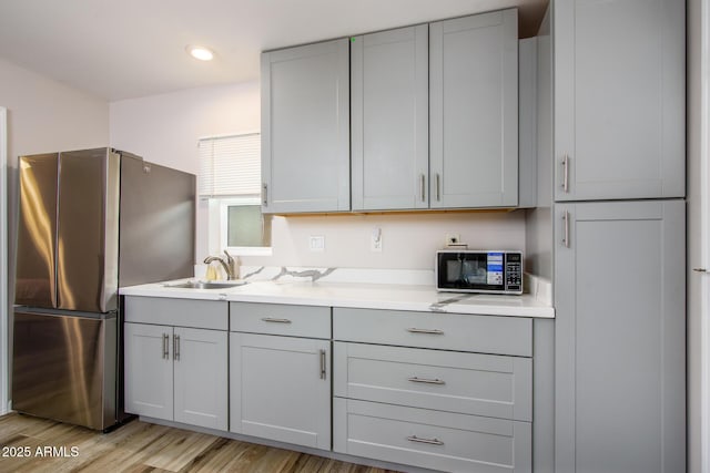 kitchen with a sink, light countertops, gray cabinets, and freestanding refrigerator