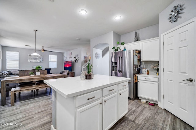 kitchen featuring hanging light fixtures, stainless steel fridge, white cabinetry, a center island, and light wood-type flooring