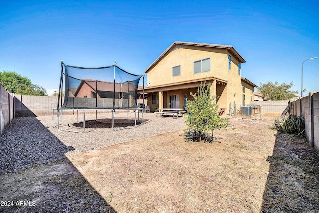 back of house with cooling unit, a trampoline, and a patio area