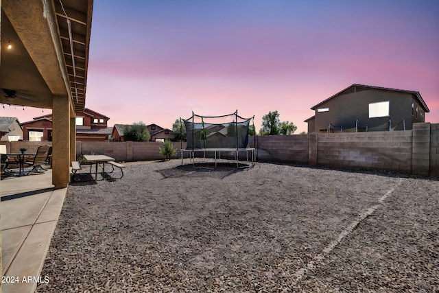 yard at dusk with ceiling fan, a trampoline, and a patio