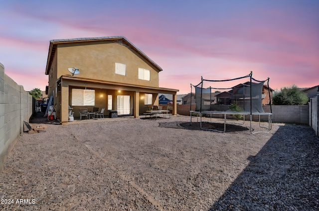 back house at dusk featuring a trampoline and a patio area