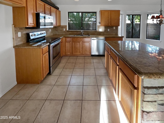 kitchen featuring dark stone counters, sink, light tile patterned floors, appliances with stainless steel finishes, and a chandelier