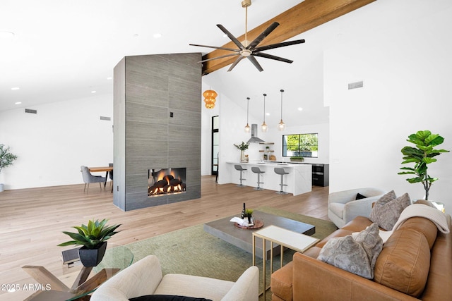 living area with a tiled fireplace, visible vents, ceiling fan, high vaulted ceiling, and wood finished floors
