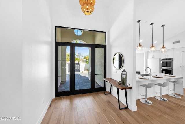 entrance foyer with high vaulted ceiling, light wood-style floors, visible vents, and baseboards