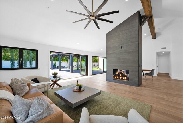 living area with high vaulted ceiling, beamed ceiling, a fireplace, light wood-type flooring, and a ceiling fan
