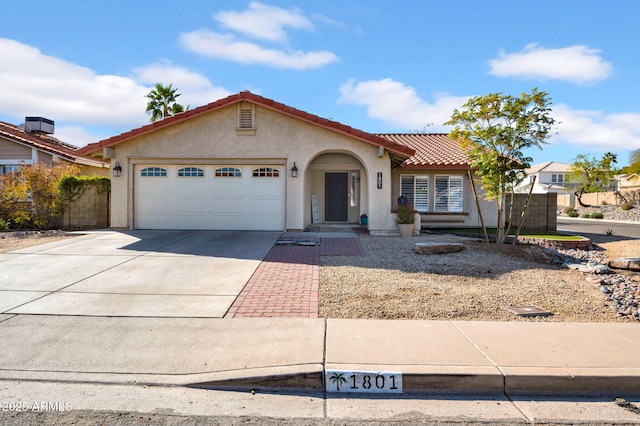 mediterranean / spanish-style house with a garage, concrete driveway, a tiled roof, fence, and stucco siding