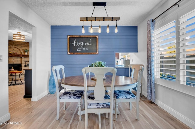 dining room with a healthy amount of sunlight, a fireplace, a textured ceiling, and wood finished floors