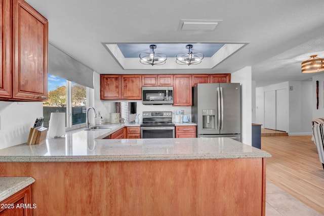 kitchen with a tray ceiling, visible vents, appliances with stainless steel finishes, a sink, and a peninsula