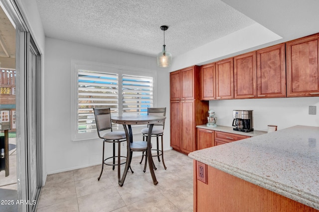 kitchen featuring hanging light fixtures, light stone counters, brown cabinets, and a textured ceiling