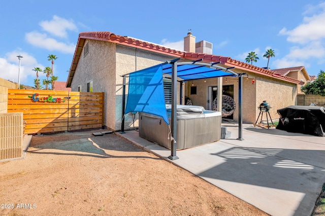 rear view of house with fence, a tiled roof, stucco siding, a patio area, and a hot tub