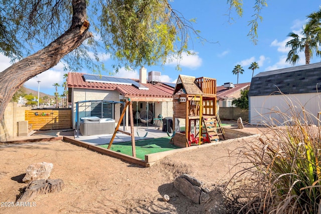 back of property with a tile roof, a playground, stucco siding, solar panels, and a fenced backyard