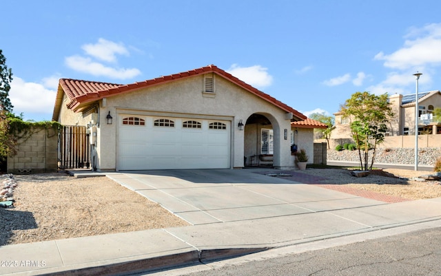 mediterranean / spanish home with a garage, driveway, a tiled roof, and stucco siding