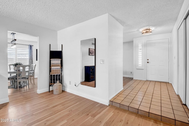 foyer entrance featuring light wood-type flooring, baseboards, and a textured ceiling