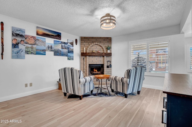 living room with a textured ceiling, a brick fireplace, light wood-style flooring, and baseboards