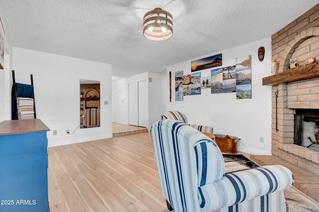 living area featuring a textured ceiling, a fireplace, wood finished floors, and baseboards