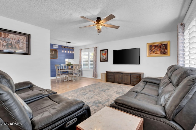 living room featuring ceiling fan, light wood finished floors, and a textured ceiling