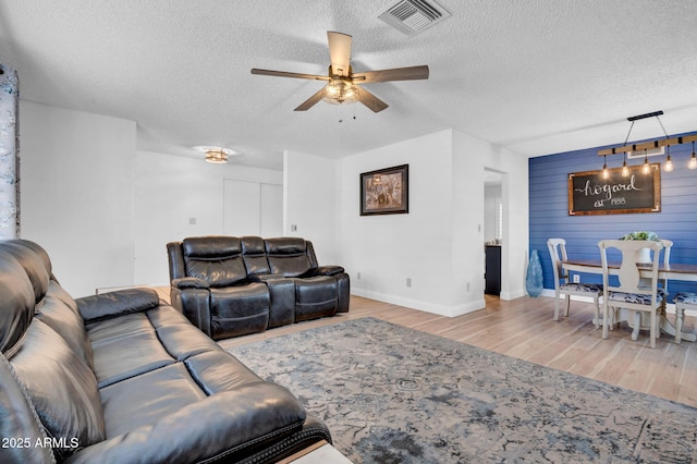 living area with visible vents, a ceiling fan, a textured ceiling, wood finished floors, and baseboards