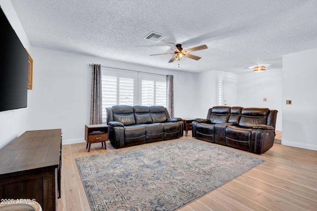 living room featuring ceiling fan, light wood-style flooring, visible vents, and baseboards