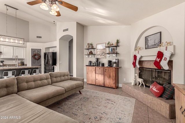 tiled living room with high vaulted ceiling, ceiling fan, sink, and a tile fireplace