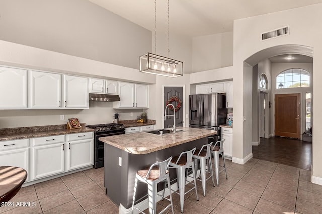 kitchen with pendant lighting, a center island with sink, sink, stainless steel refrigerator with ice dispenser, and black gas range oven