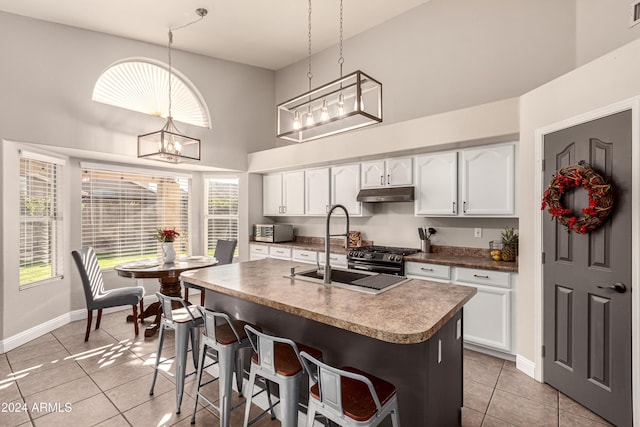 kitchen featuring white cabinetry, light tile patterned floors, hanging light fixtures, and an island with sink