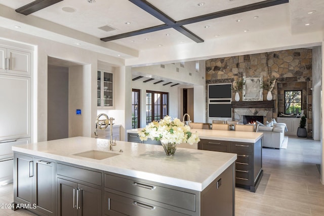 kitchen featuring a kitchen island with sink, light wood-type flooring, a fireplace, beam ceiling, and sink