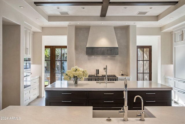 kitchen with backsplash, appliances with stainless steel finishes, wall chimney range hood, and an island with sink