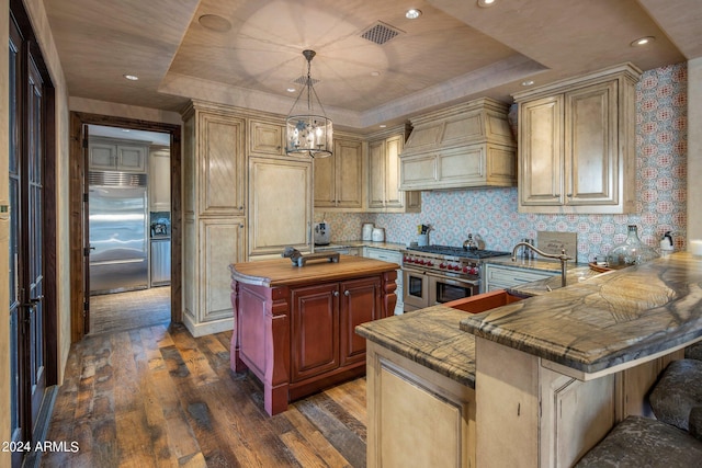 kitchen featuring high end appliances, dark hardwood / wood-style flooring, a tray ceiling, custom range hood, and a kitchen bar