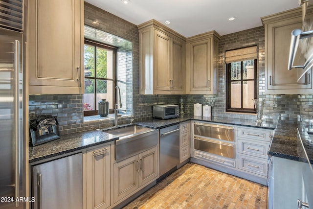 kitchen with appliances with stainless steel finishes, tasteful backsplash, dark stone counters, and sink